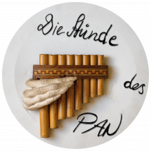 Foto von einer Panflöte, die von einer geschnitzten Hand gehalten wird mit der Aufschrift "die Stunde des Pans"